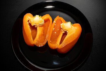 Orange bell pepper, half and slices isolated on black plate. Concept food preparation process.