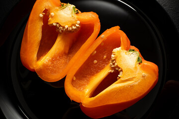 Orange bell pepper, half and slices isolated on black plate. Concept food preparation process.