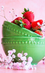 Fresas frescas en cuencos de cerámica verde y flores de gypsophila. Fondo rosa.