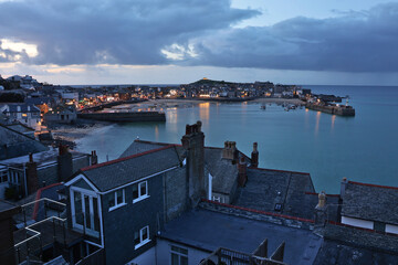 Moody early evening view over St Ives Harbour during high tide with reflections and illuminated...