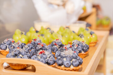 A colorful and delicious buffet spread featuring a wide variety of international dishes, including fizzy cola, lemon tart, creamy cheesecake, blueberry tart, crispy fried chicken, and savory pasta