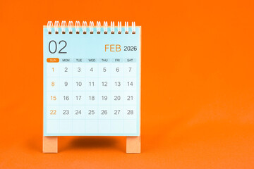 February 2026 desk calendar stand on orange color textile background.