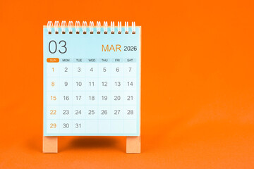 March 2026 desk calendar stand on orange color textile background.