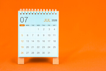July 2026 desk calendar stand on orange color textile background.