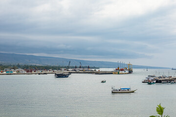 Fototapeta premium Sumba, Indonesia – 07. 04. 2025 – It's still daytime, but the weather is cloudy. Two seaports in Waingapu are visible in a single view, with small and large ships moored around them