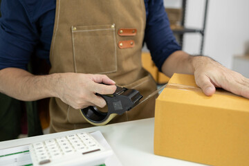 A man is packing things into boxes. He uses scotch tape and string to tie the boxes, writes...
