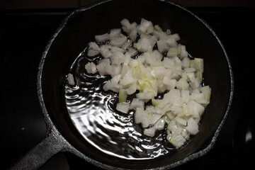Home cooking. Onions are fried in a cast iron skillet on a hot pan with vegetable oil. Close-up.