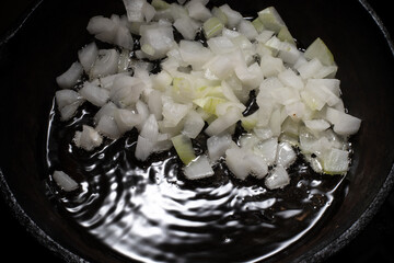 Home cooking. Onions are fried in a cast iron skillet on a hot pan with vegetable oil. Close-up.