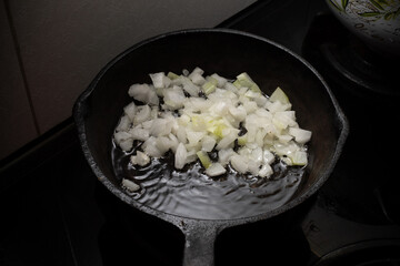 Home cooking. Onions are fried in a cast iron skillet on a hot pan with vegetable oil. Close-up.