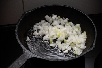 Home cooking. Onions are fried in a cast iron skillet on a hot pan with vegetable oil. Close-up.