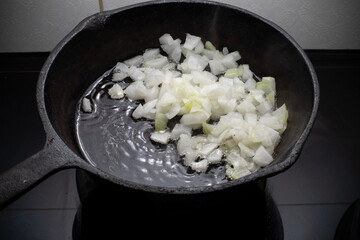 Home cooking. Onions are fried in a cast iron skillet on a hot pan with vegetable oil. Close-up.