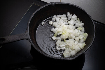 Home cooking. Onions are fried in a cast iron skillet on a hot pan with vegetable oil. Close-up.