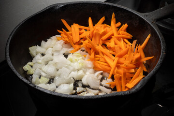 Home cooking. On the stove in a cast iron frying pan onions and carrots are fried in a hot frying...