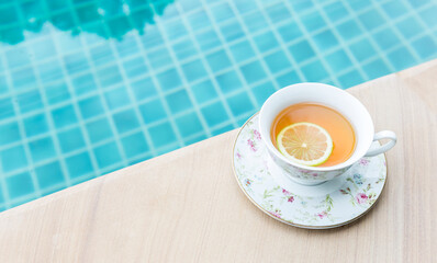 Hot tea with lemon slice in flower tea cup on swimming pool edge, hot drink, healthy drink