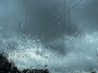 Raindrops streak across a window, blurring the view of a dramatic, overcast sky, evoking a sense of...
