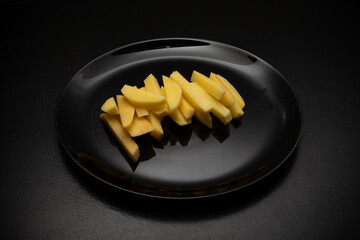 Raw potatoes cut into large strips on a black plate, top view, side view. Cooking delicious French...