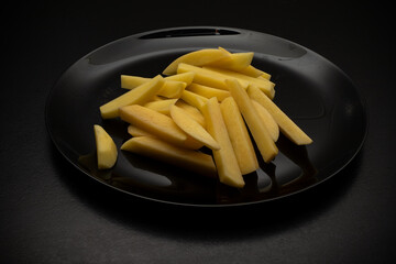 Raw potatoes cut into large strips on a black plate, top view, side view. Cooking delicious French fries. Homemade food. French fries