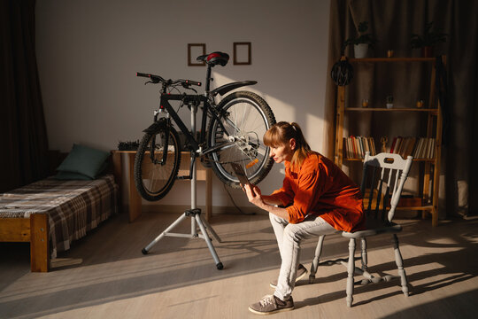 Female cyclist repairing bicycle at home while using digital tablet searching advices in internet