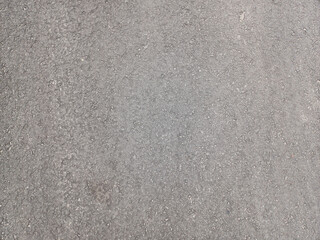 Textured, light gray asphalt or concrete surface, dotted with small, dark specks, showing a rough, granular ground material. Related to textures, construction materials, road surfaces, backgrounds
