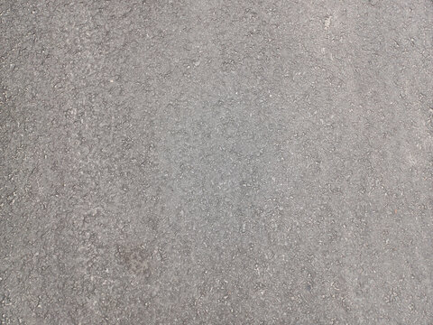 Textured, light gray asphalt or concrete surface, dotted with small, dark specks, showing a rough, granular ground material. Related to textures, construction materials, road surfaces, backgrounds