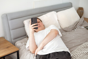 Teen boy checking social media holding smartphone, using mobile phone app playing game, relaxing on...