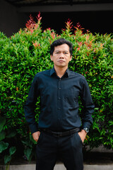 Portrait of a man in black shirt posing in front of lush greenery, professional attire style