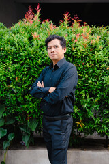 Portrait of a confident asian man with arms crossed, standing in front of vibrant foliage
