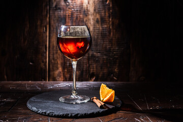 Glass of wine on a slate tray. Glass of wine on a wooden background. Cinnamon and orange slices. Serving wine.