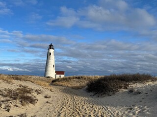 A lighthouse on a beach in Nantucket during golden hour, with warm sunlight casting long shadows...