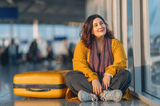 Modern plus size woman sitting confidently at airport gate with luggage waiting for her flight