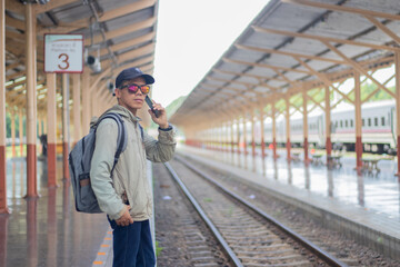 Young man standing alone at sunrise, standing on train station platform, holding map, confused but...