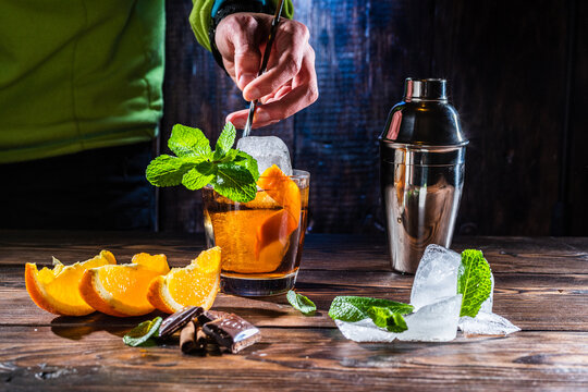 Mixing a cocktail with a bartender's spoon. Bartender mixes a cocktail. Large pieces of ice and mint in a glass. Spoon in hand.