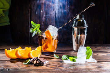 Cocktail with ice and orange. Cocktail spoon in a glass. Orange slices and chocolate in the...