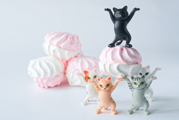  Cute toy kittens joyfully lifting pink and white marshmallows in a playful scene set against a...