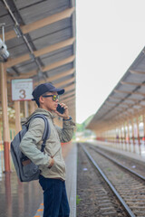Fototapeta premium Young man standing alone at sunrise, standing on train station platform, holding map, confused but inspired, travel, direction, exploration, journey, freedom, lifestyle, waiting, seriousness, sunlight