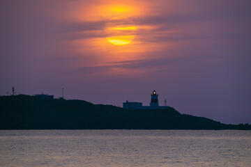The iconic Fuguijiao Lighthouse stands silhouetted against a vibrant sunset sky in Shimen District...