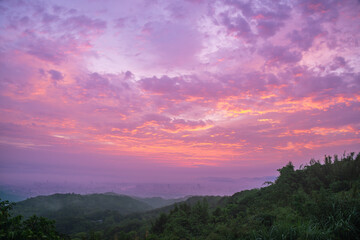 A breathtaking sunset paints the sky with vibrant hues over the lush mountains of Shulin District New Taipei City Taiwan, with a faint cityscape visible in the distance.