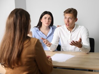 Couple complaining to woman at wooden table indoors