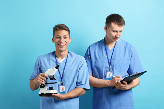 Medical students with microscope and clipboard on light blue background