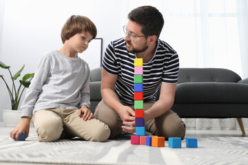 Father and his son playing with colorful cubes on floor at home, low angle view