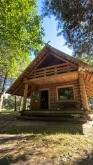 Rustic wooden cabin nestled among tall trees, featuring a sloped roof and large windows, surrounded...