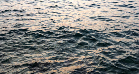 close-up of calm sea water surface under soft sunset light with gentle waves and sunlight reflection. aesthetic background with