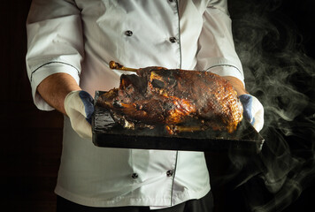 A chef in a white uniform holds a perfectly roasted duck on a black platter in a professional...