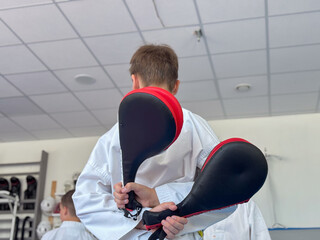 a person with their back to the camera holding two martial arts training pads, facing a white wall...