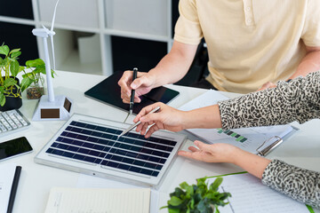 Asian business adults analyze renewable energy ESG solutions with solar panel and wind turbine...