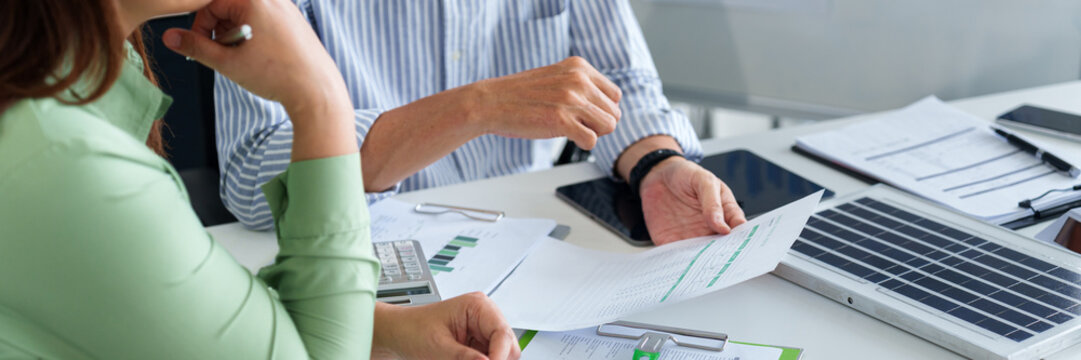 Business professionals analyzing sustainable finance reports and ESG strategies during a corporate meeting focusing on renewable energy investments - Powered by Adobe
