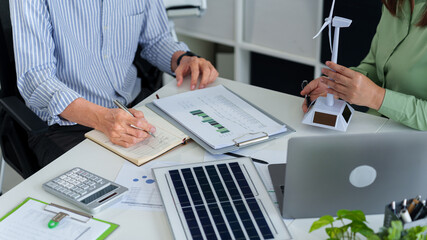 Adult Asian professionals collaboratively examine renewable energy solutions corporate...
