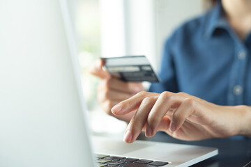 Woman using credit card and laptop computer for internet banking and online shopping at home,...