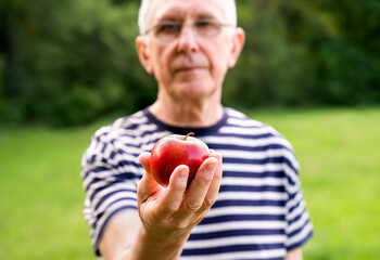 Mature man gives a ripe red apple. Healthy nutrition concept. Selective focus.