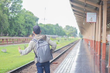 Young man standing alone at sunrise, standing on train station platform, holding map, confused but...